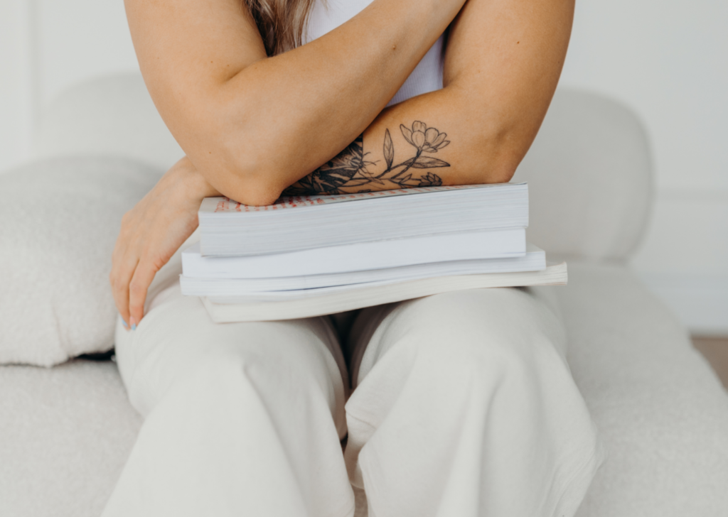 Web and brand designer from Hamilton, Ontario, expressing a clear point of view while sitting on a white couch wearing all white with her arms crossed on a stack of books