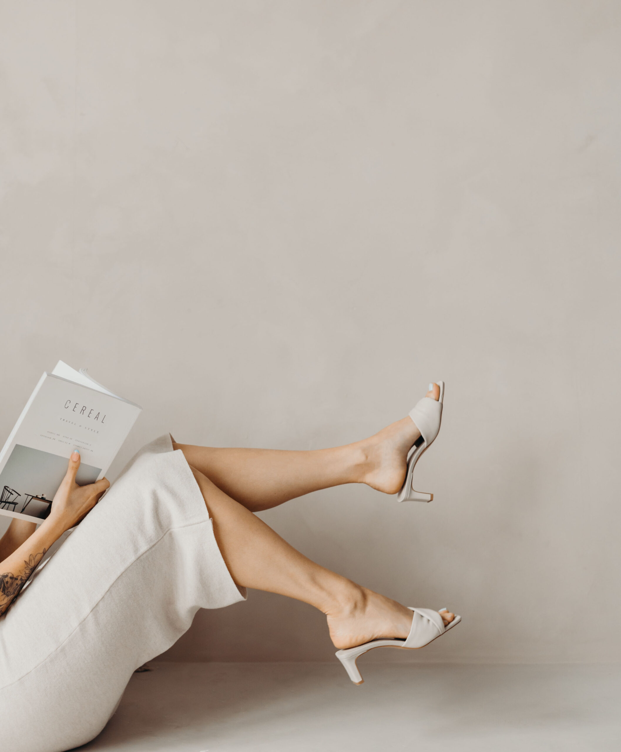 Relaxed business woman in a beige outfit with her feet up, reading a magazine.